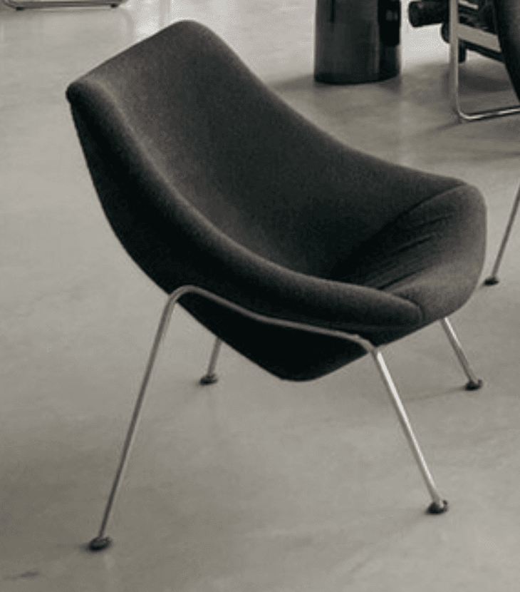 A modern lounge chair featuring a continuously curved, dark gray upholstered shell seat and back, supported by four slender, splayed polished metal legs. — 3D model