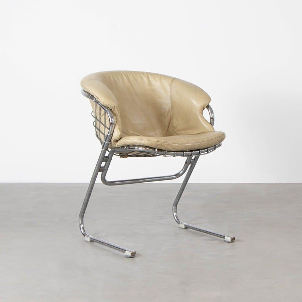 A contemporary accent chair with a chrome-plated tubular metal frame and a cantilevered base. The seat and backrest are upholstered in light tan leather, contoured to provide a relaxed seating posture. The backrest features a wire mesh support structure. — 3D model