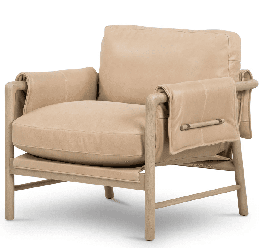 A contemporary armchair with a light beige leather upholstery and a light wood frame. The armchair features a deep seat, a supportive backrest, and padded armrests. The frame has a minimalist design with visible joinery and leg structure. A notable design element is the leather flap draped over each armrest, secured with a metal buckle-like accent. — 3D model