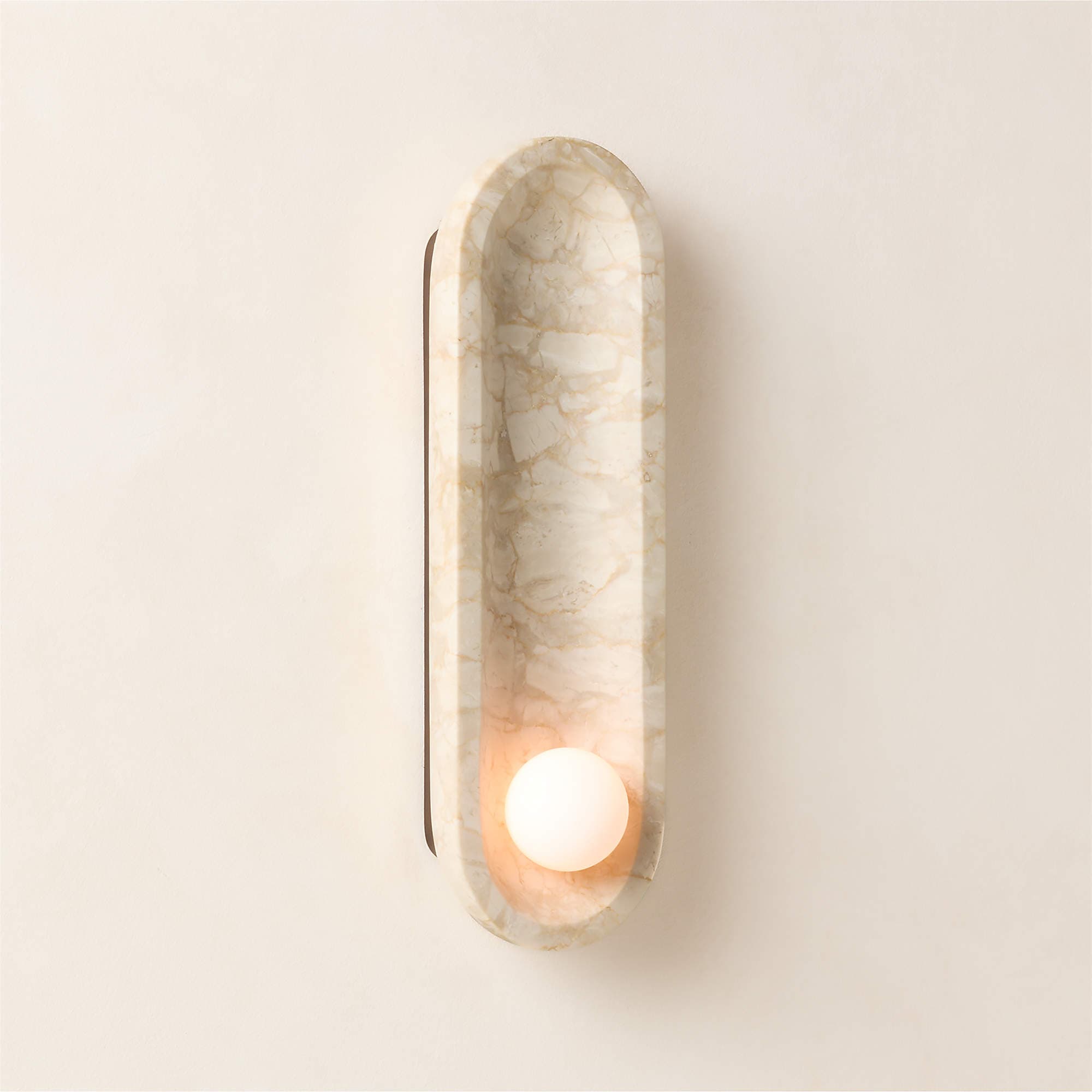 A contemporary wall-mounted light fixture featuring an elongated, pill-shaped body crafted from light-toned, veined marble. A single spherical, opaque light bulb is recessed within the lower section of the marble form, emitting a soft, warm, and diffused glow. — 3D model