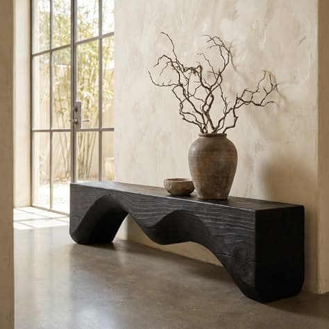 A long, dark-colored bench with a distinctive undulating, sculptural form. The bench appears to be carved from a solid piece of wood, showcasing a prominent wood grain texture that has been accentuated by a dark finish, possibly burnt or stained. The design is organic and modern, with curved supports creating a dynamic silhouette. — 3D model