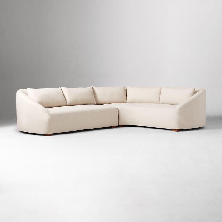 A sectional sofa with a curved design, upholstered in a light-colored fabric. It features multiple seating cushions and back cushions, forming an L-shape configuration. The arms are rounded and integrated into the overall form. — 3D model