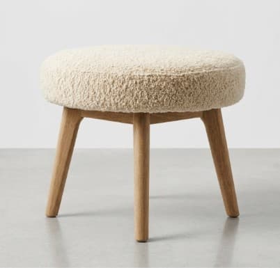 A round stool with a plush, textured seat and three tapered wooden legs. — 3D model