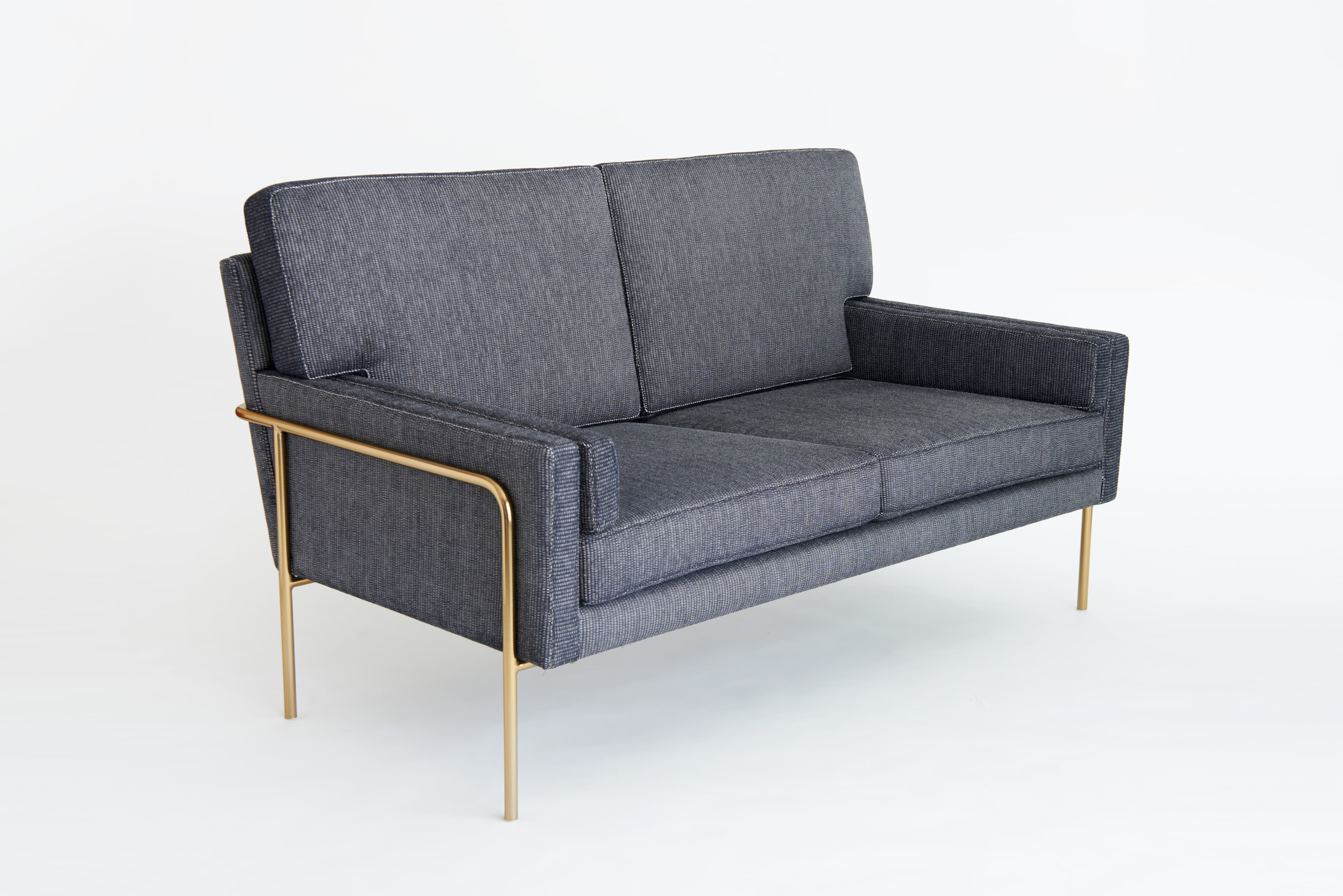 A two-seater sofa with a modern design. The sofa features a rectangular frame upholstered in dark gray textured fabric. It has a straight backrest divided into two cushions and a seat cushion. The arms are integrated into the frame, and a distinctive feature is the polished gold-colored metal frame that extends from the arms and supports the sofa on thin, angled legs. The metal frame has a sleek, minimalist profile. — 3D model