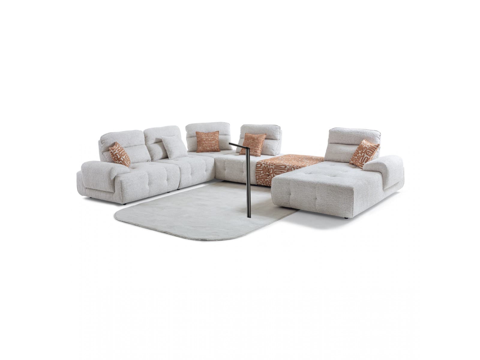 A modular sectional sofa with multiple seating units, including a chaise lounge. The sofa features a textured, boucle-like upholstery in a light, neutral color. The backrests are composed of several individual cushions, and the seats have a tufted design. Accent pillows with an abstract geometric pattern in shades of orange and brown are placed on the sofa. A low-profile, rectangular ottoman with a similar patterned upholstery is positioned in front of a portion of the sofa. A slender, dark-colored floor lamp with a minimalistic design is placed between sofa sections. — 3D model